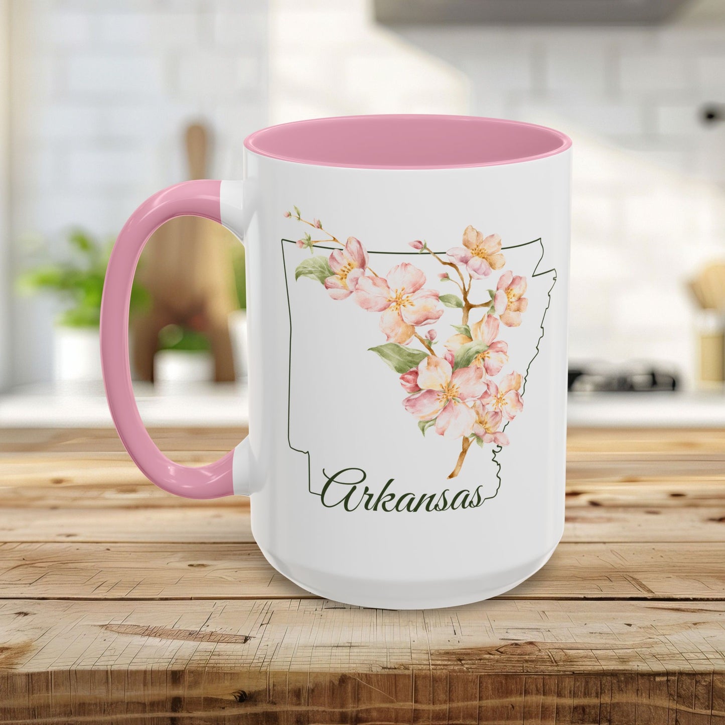 White ceramic mug with pink handle and interior, featuring watercolor apple blossoms over an Arkansas outline.