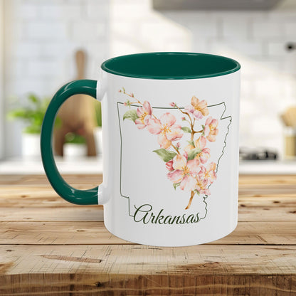 White ceramic mug with teal handle and interior, featuring a watercolor Arkansas map with pink apple blossoms.