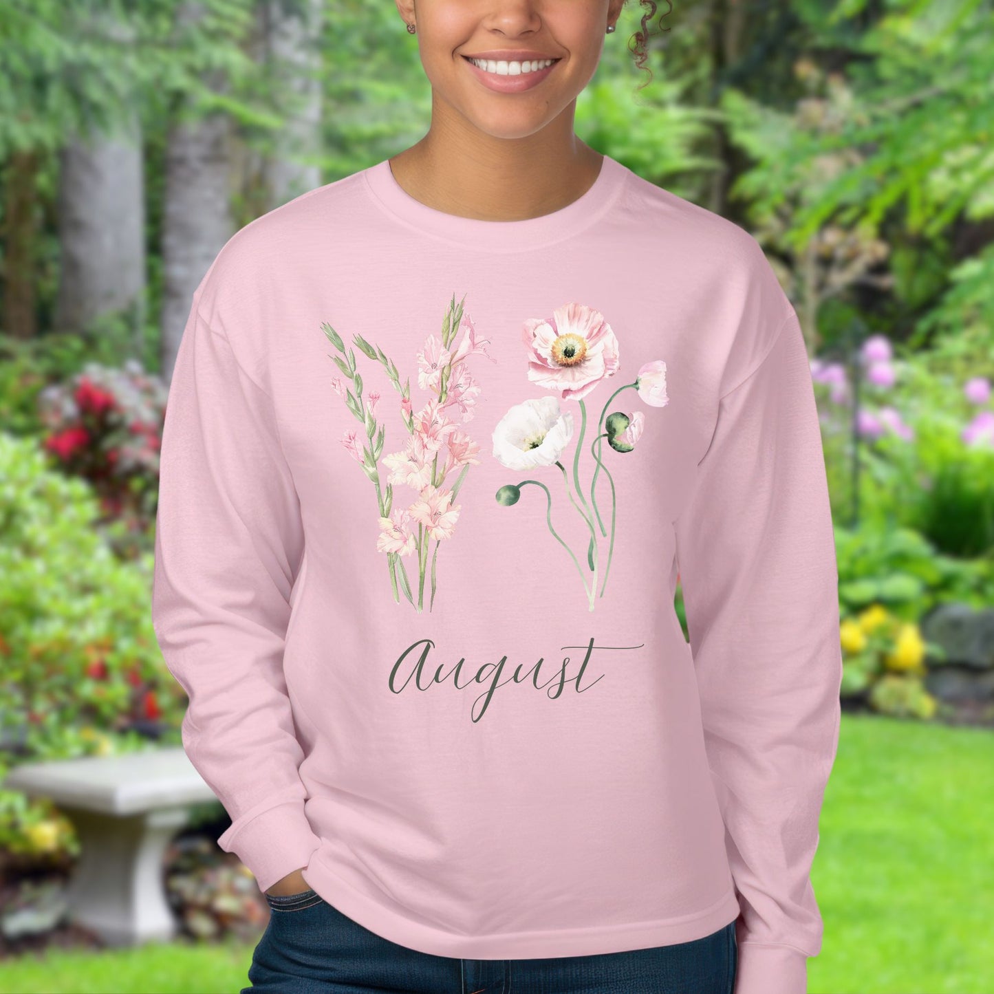 Pink long-sleeve tee with watercolor gladiolus and poppy blooms, "August" script, worn by a smiling woman.