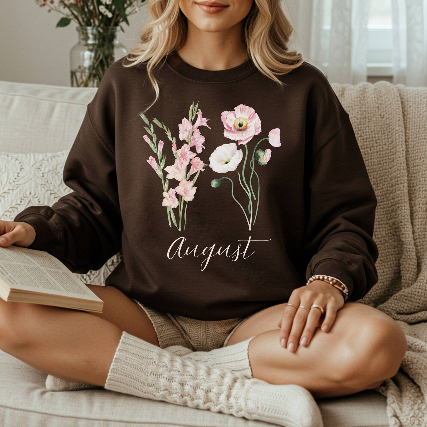 Woman wearing a brown August birth month flower sweatshirt with watercolor gladiolus and poppy blooms.