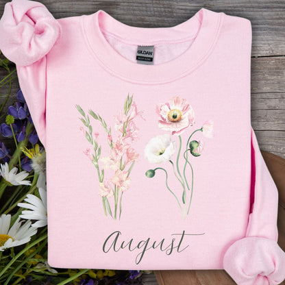 Light pink Gildan sweatshirt with watercolor gladiolus and poppy flowers, "August" text, on wood with flowers.