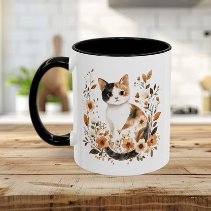 White ceramic mug with black handle and interior, featuring a watercolor calico cat surrounded by autumnal florals.