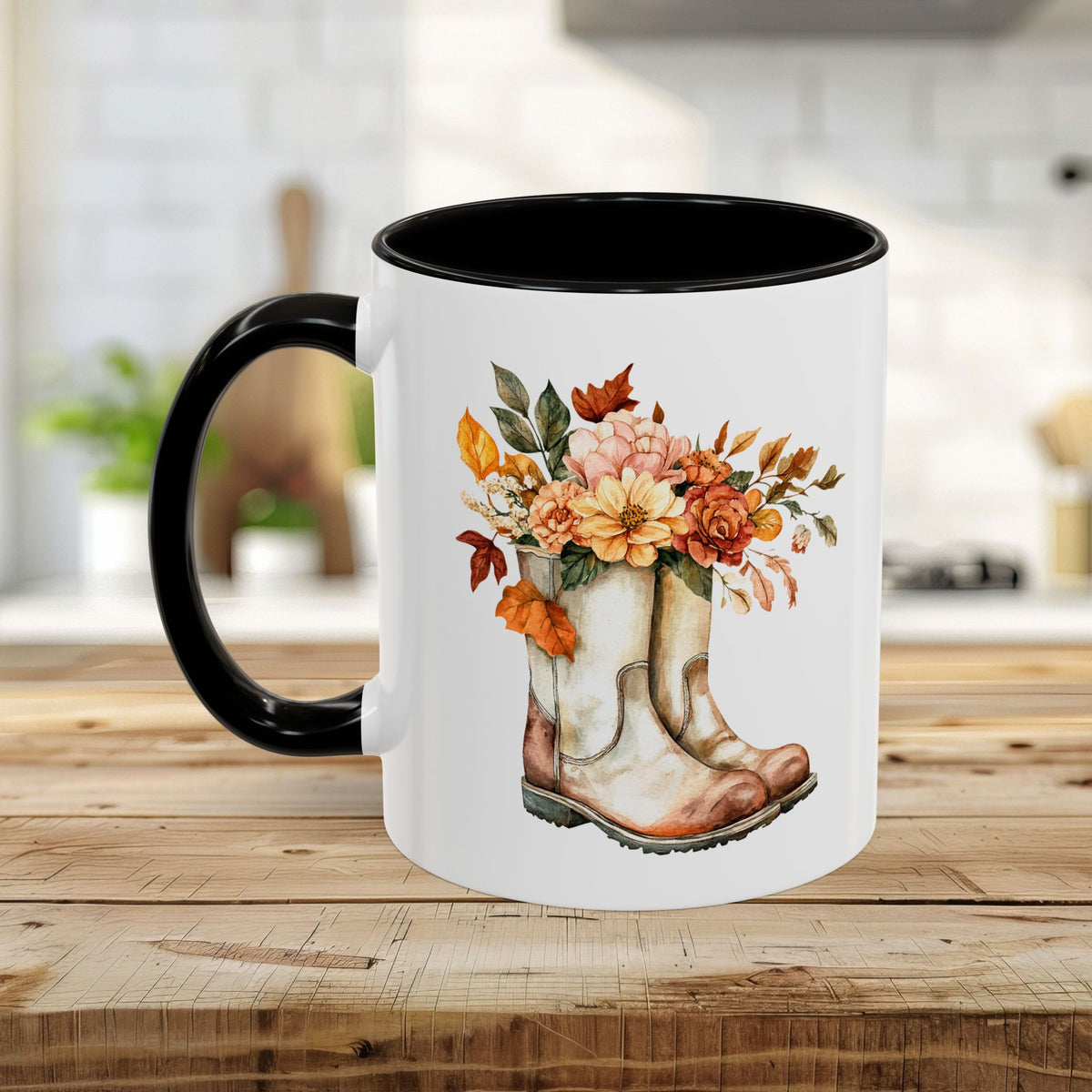 White ceramic mug with black handle and interior, featuring a watercolor design of worn boots overflowing with autumn flowers and leaves.