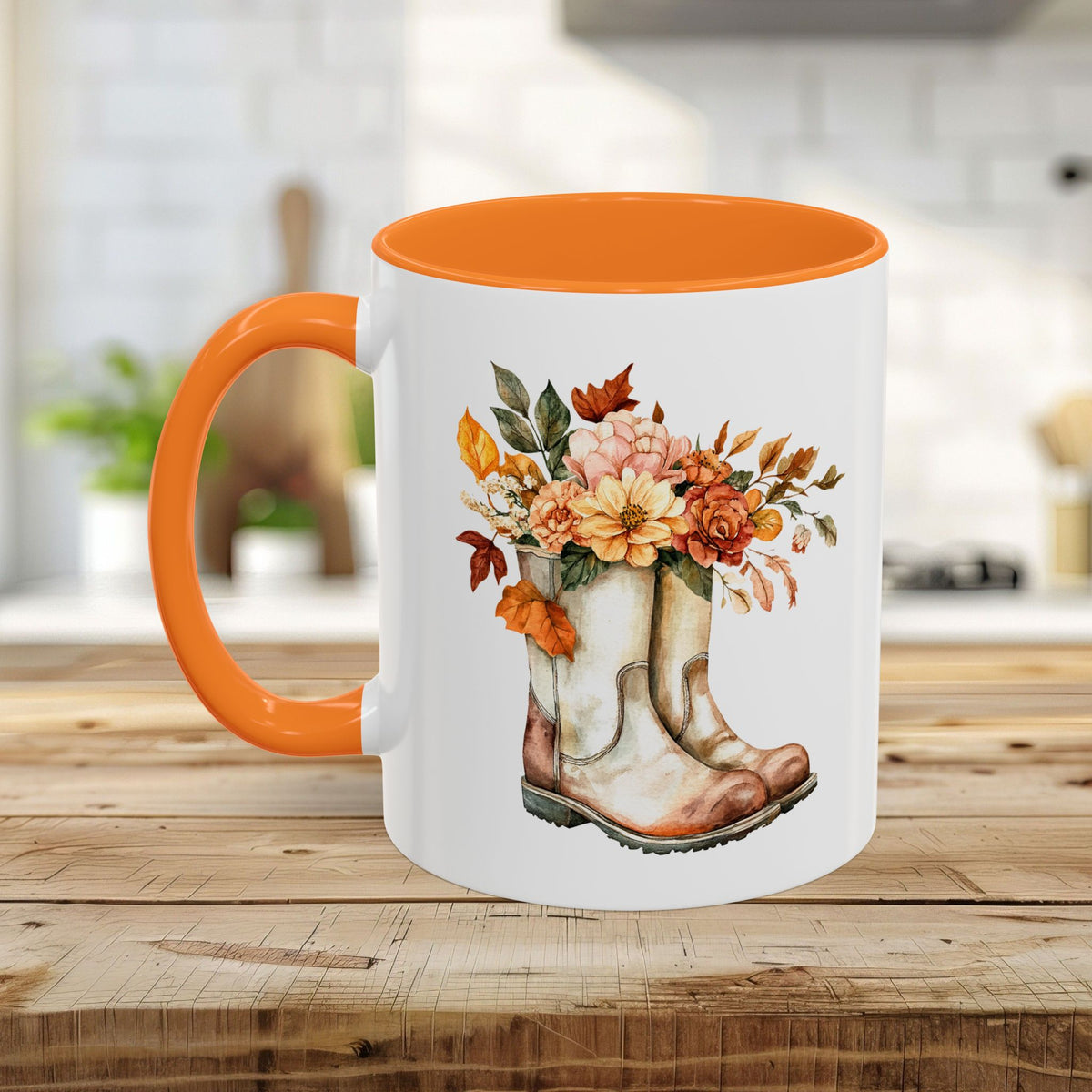 White ceramic mug with orange handle and interior, featuring a watercolor design of worn cowboy boots filled with autumn flowers.