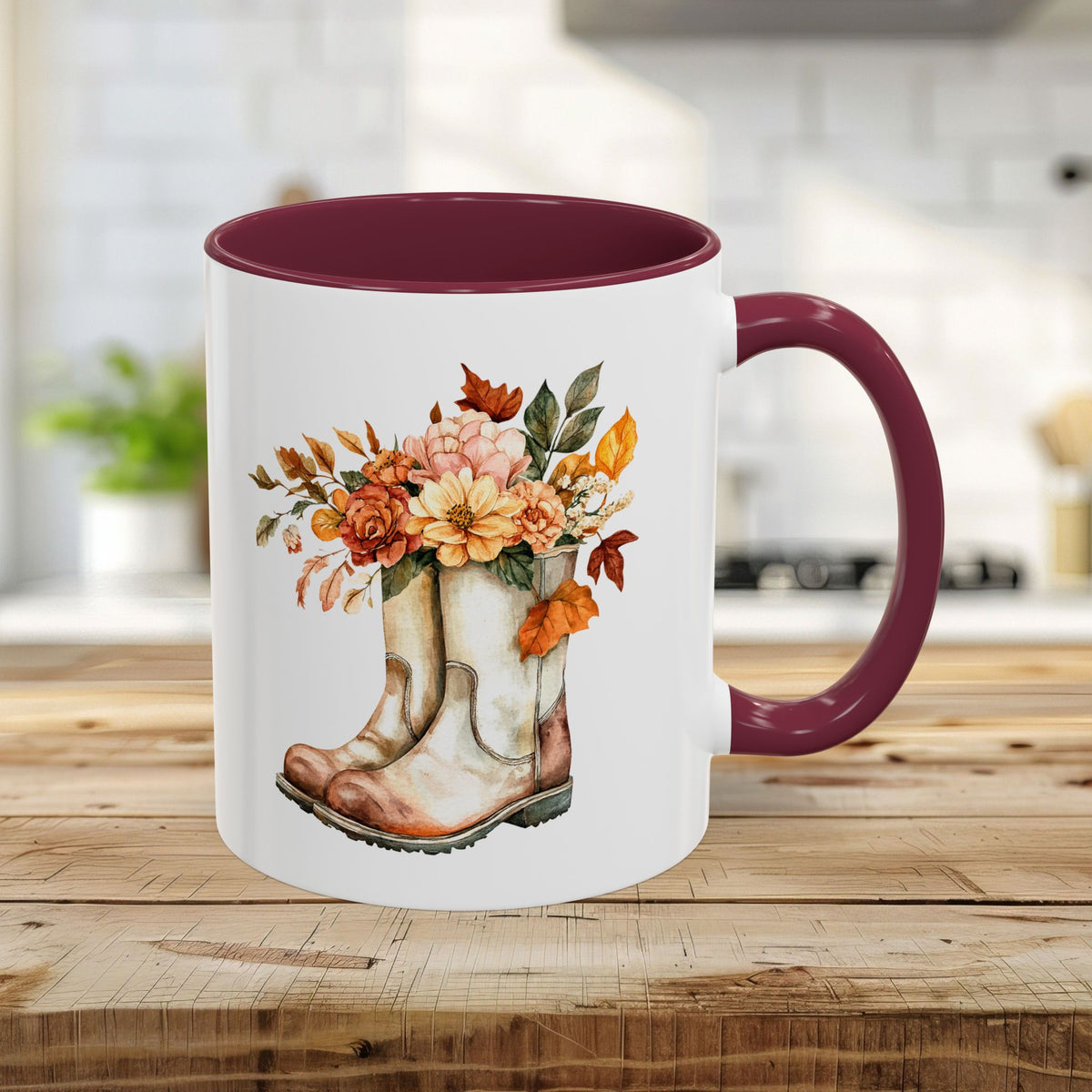 White 11oz ceramic mug with maroon handle and interior, featuring a watercolor design of worn boots overflowing with autumn flowers.