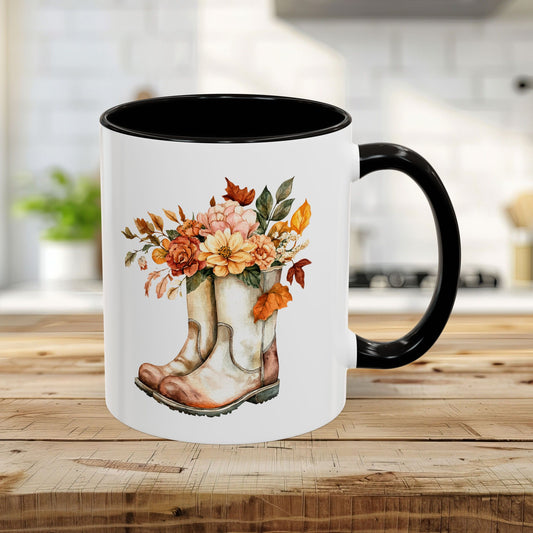 11oz white ceramic mug with black handle and interior, featuring a watercolor print of cowboy boots overflowing with autumn flowers.