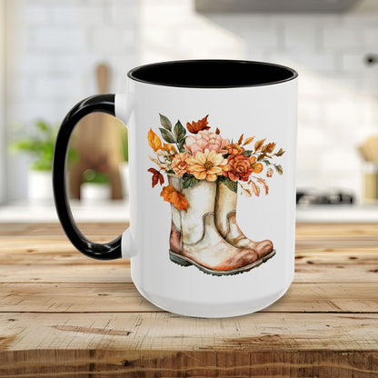 White ceramic mug with black handle and interior, featuring watercolor cowboy boots overflowing with autumn flowers.