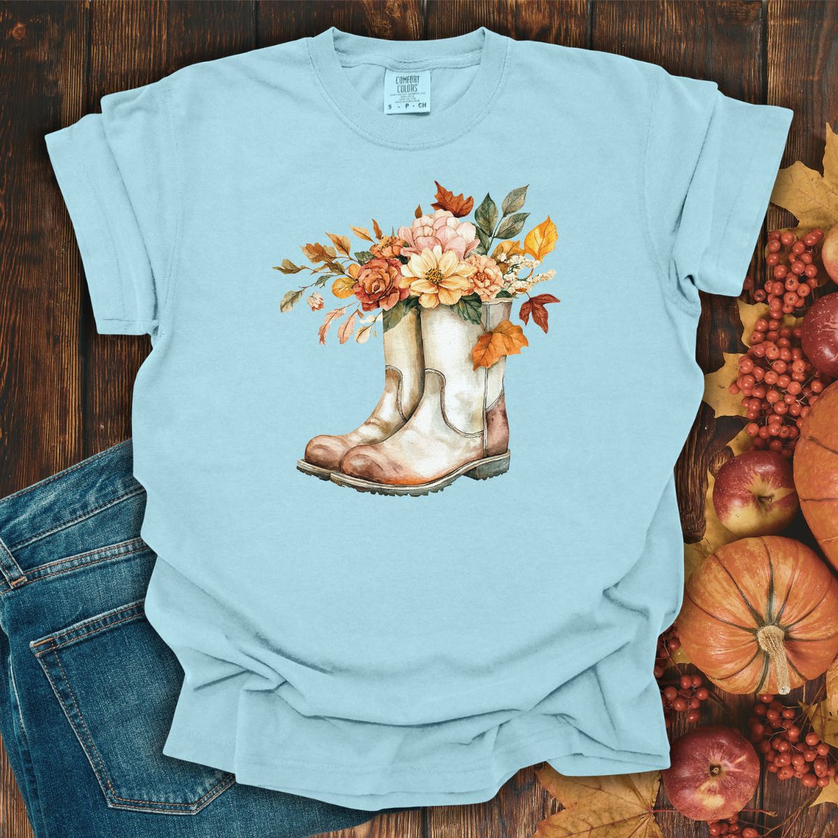 Light blue relaxed-fit tee with watercolor cowboy boots and autumn flowers, beside jeans and fall decor.