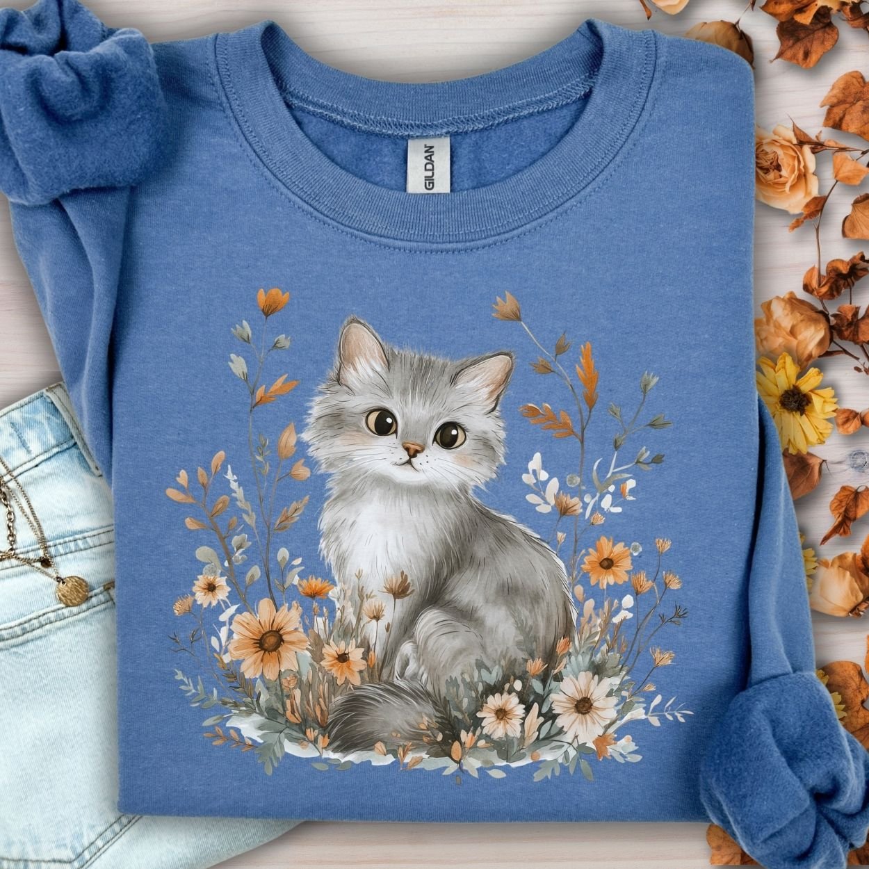 Indigo blue sweatshirt with a hand-painted grey kitten among warm autumn wildflowers.
