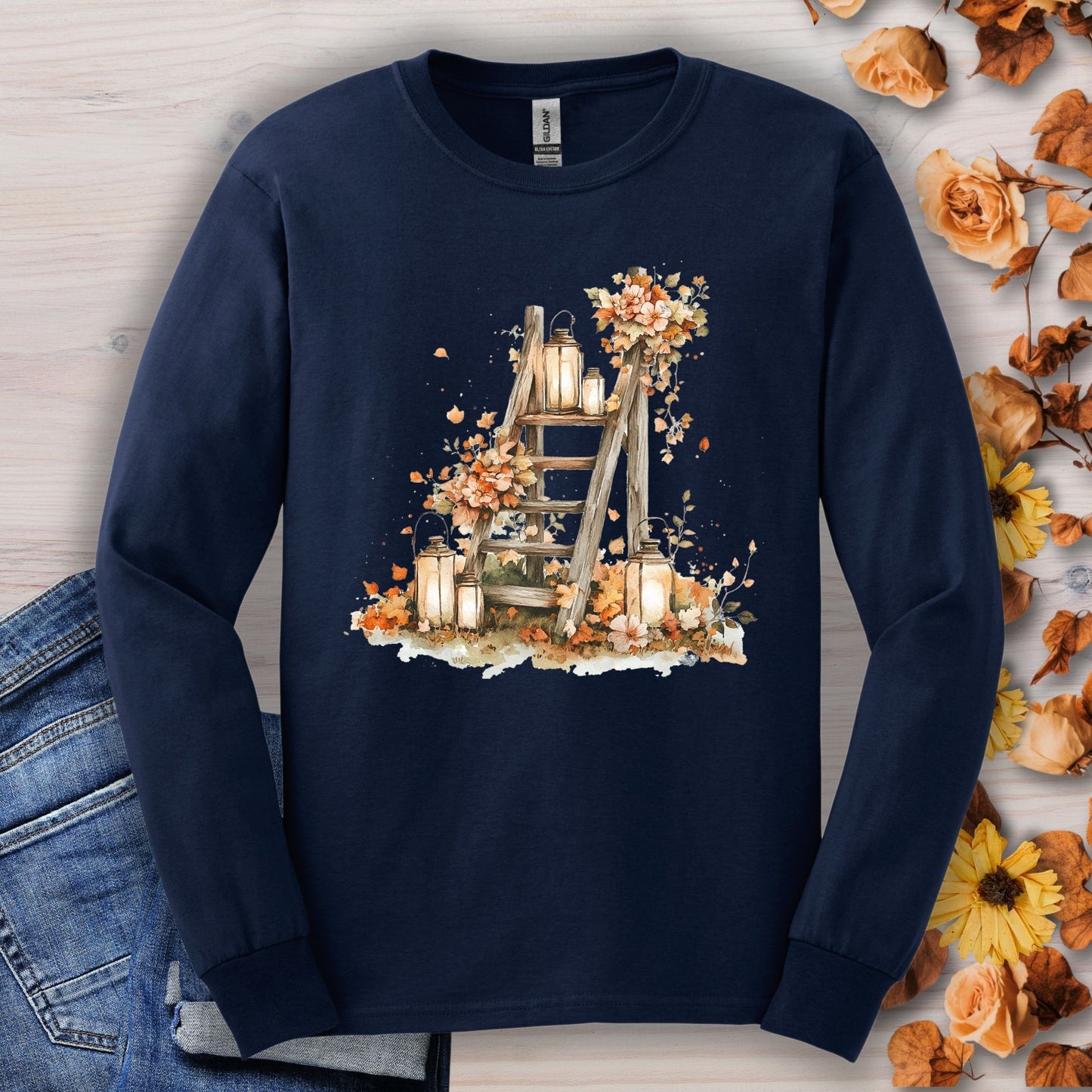 Navy long sleeve tee with watercolor autumn lanterns, flowers, and leaves on a rustic ladder.