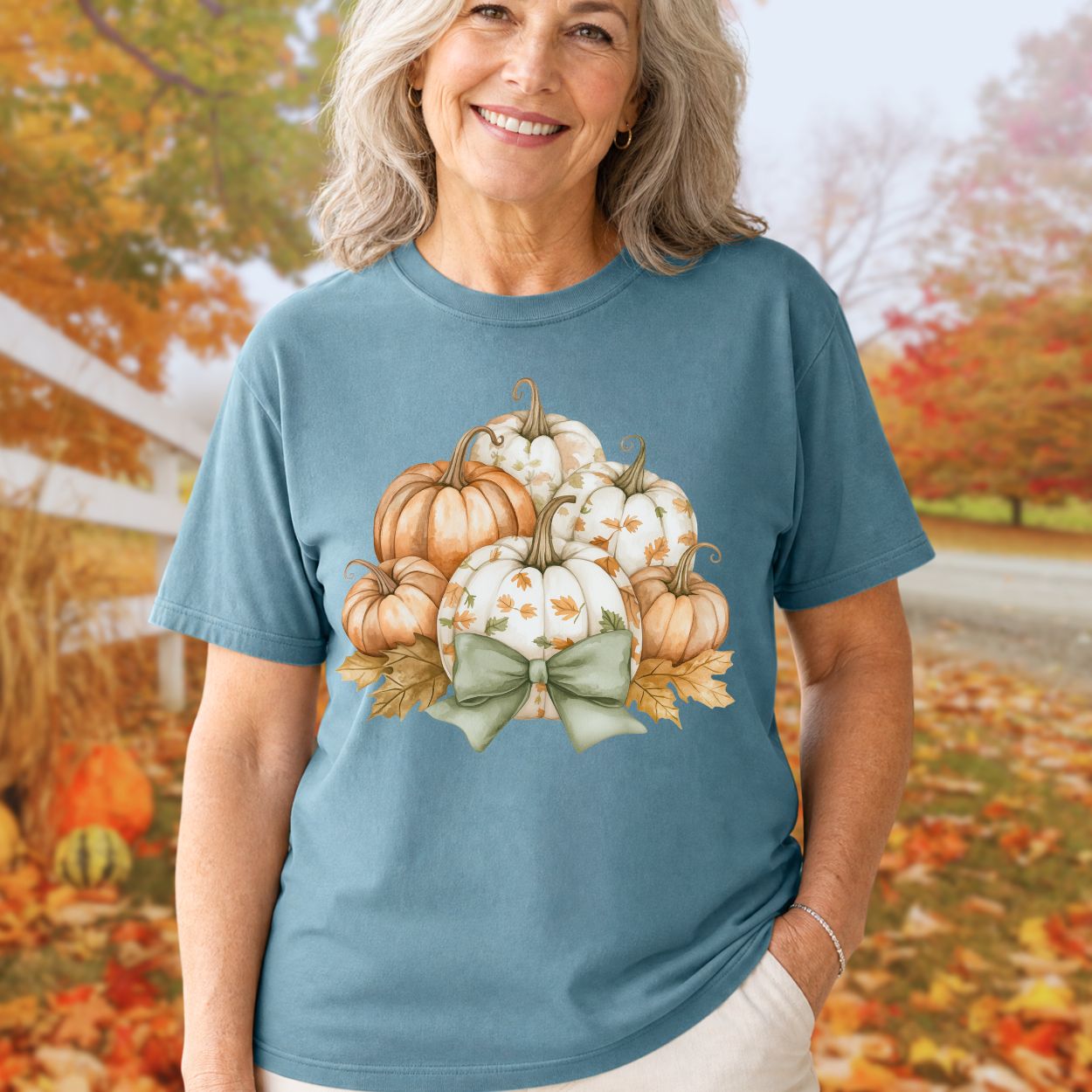 Woman in a blue Comfort Colors tee with watercolor pumpkins, autumn leaves, and a sage green bow.