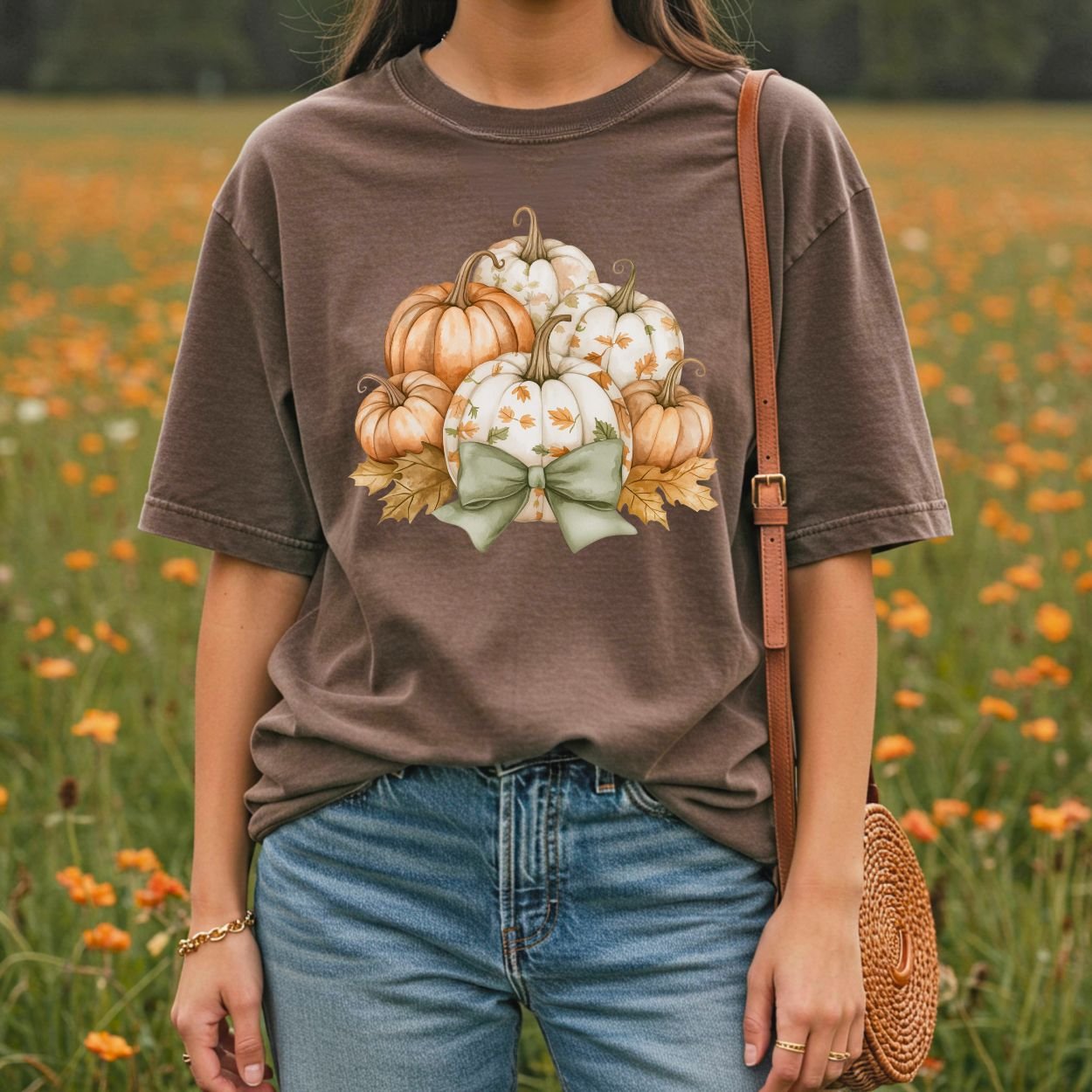 Comfort Colors brown tee with watercolor pumpkins, autumn leaves, and a green bow, worn in a field.