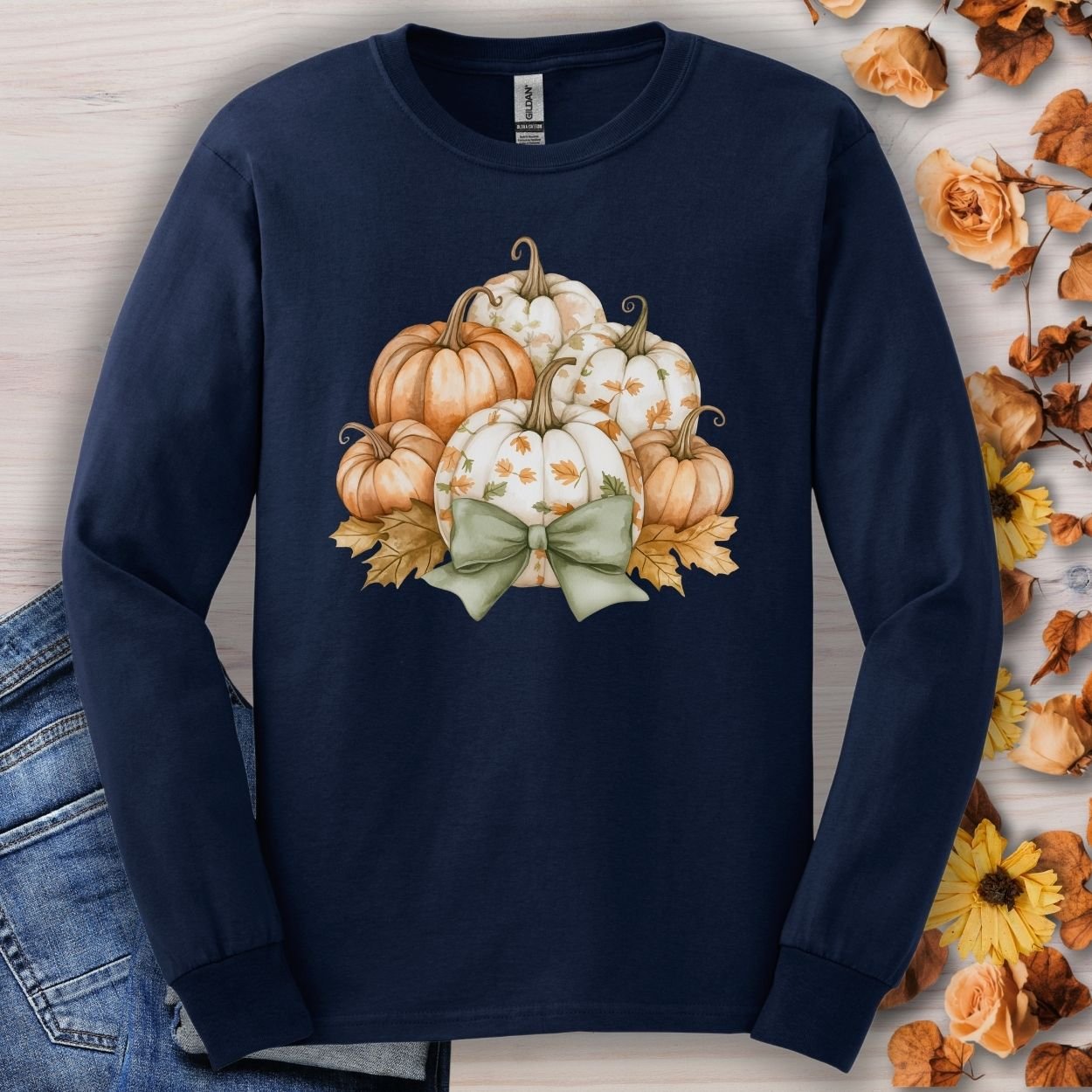 Navy long sleeve tee with a watercolor pumpkin and sage bow design, surrounded by autumn leaves.