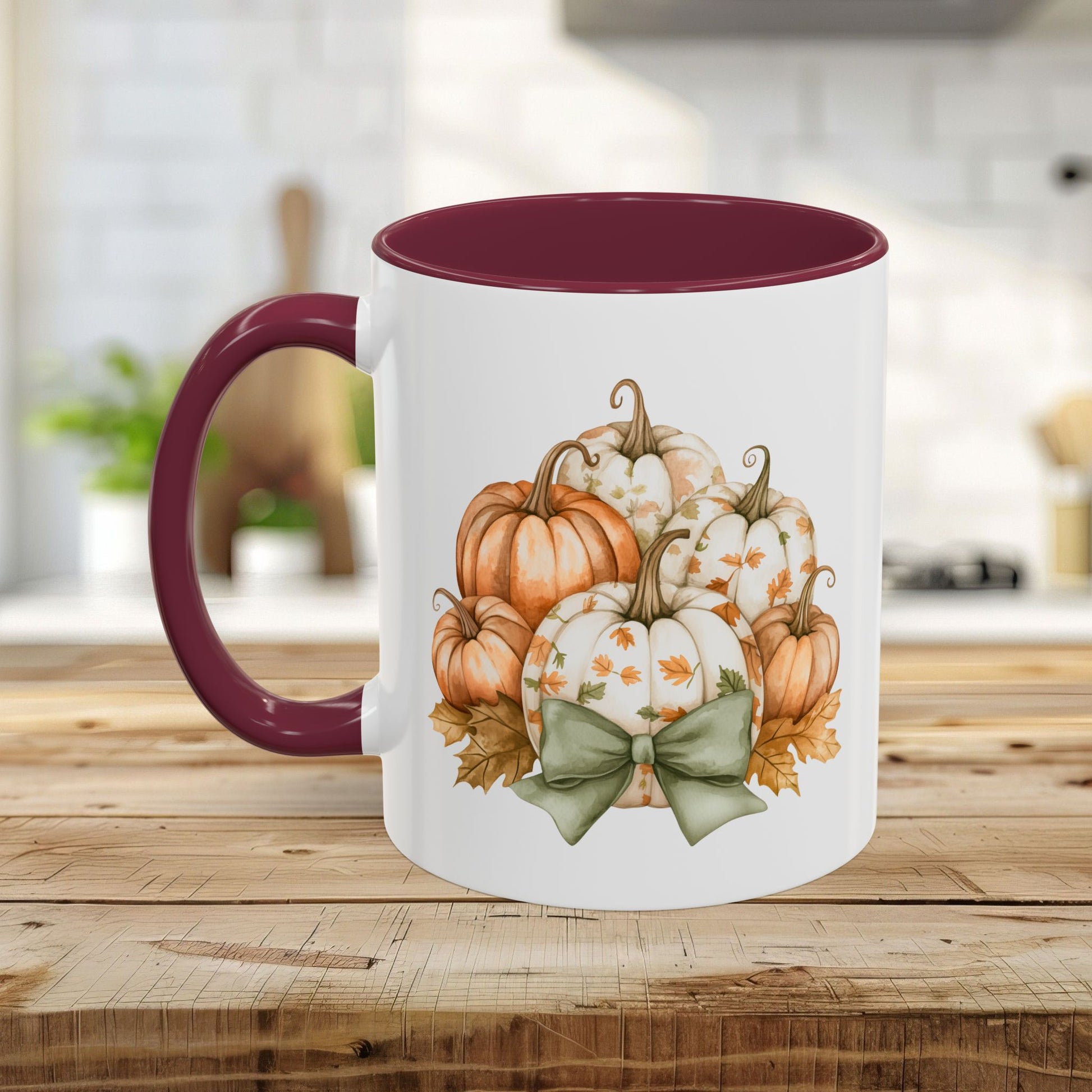 White ceramic mug with a maroon interior and handle, featuring a watercolor print of autumn pumpkins and a green bow.