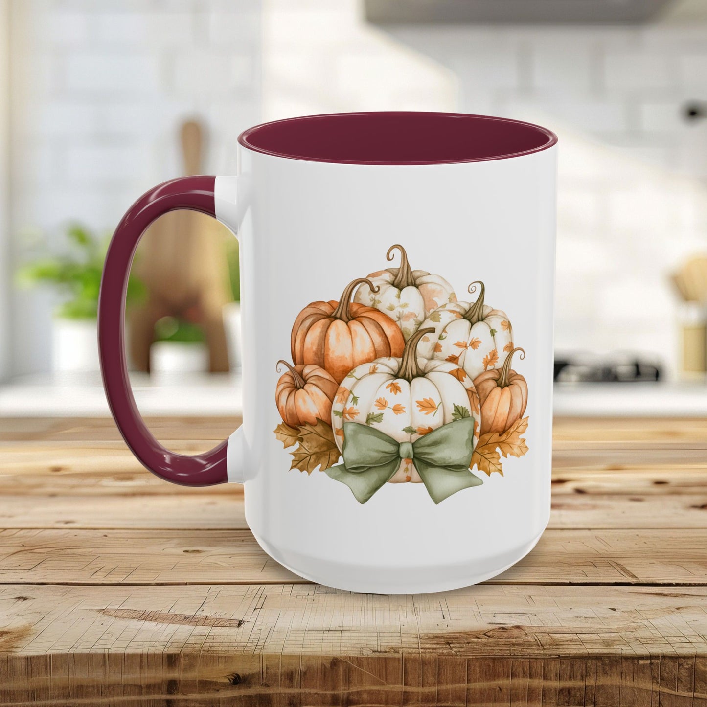 White ceramic mug with a maroon handle and interior, featuring a watercolor print of autumn pumpkins and a green bow.