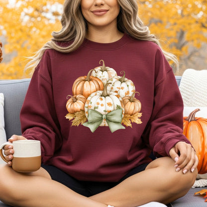 Woman in a maroon Gildan sweatshirt with a cottagecore pumpkin and green bow design, holding a mug.