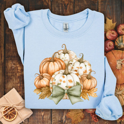Light blue Gildan sweatshirt with a cottagecore pumpkin and green bow design, surrounded by fall leaves.