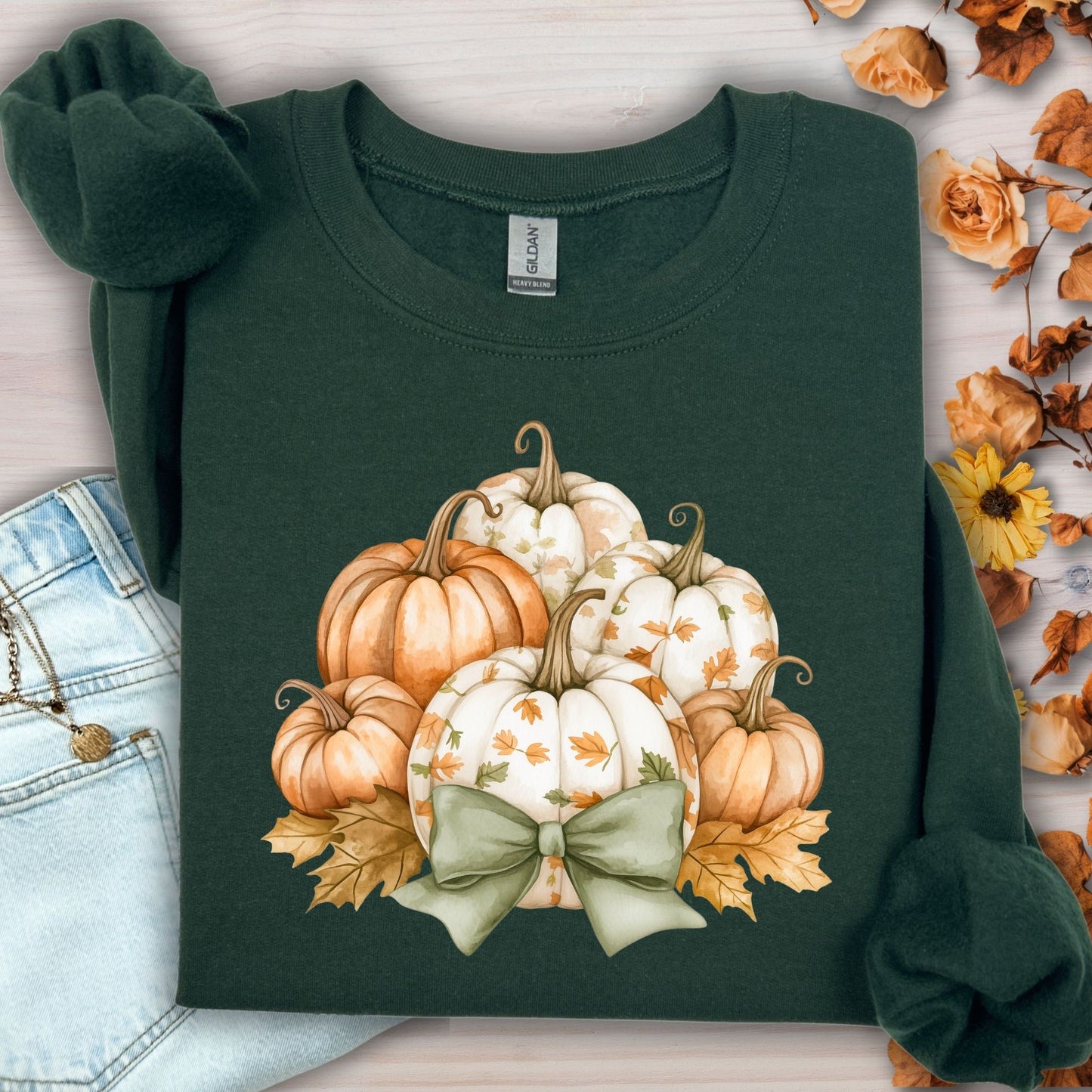 Forest green Gildan sweatshirt with a cottagecore pumpkin and green bow design, surrounded by autumn leaves.