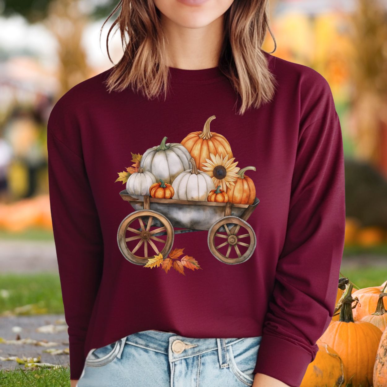 Maroon long-sleeve tee with a watercolor wagon full of white and orange pumpkins and a sunflower.
