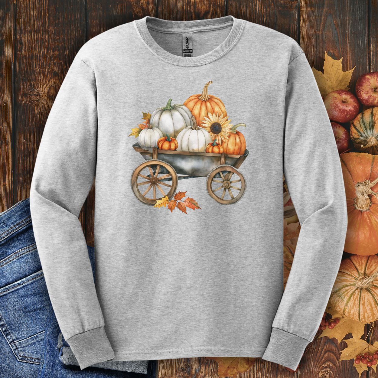 Ash long-sleeve tee with a watercolor wagon full of white and orange pumpkins, sunflower, and fall leaves.