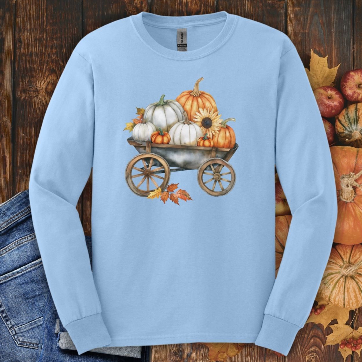 Light blue long sleeve tee with a watercolor wagon full of white and orange pumpkins and fall leaves.
