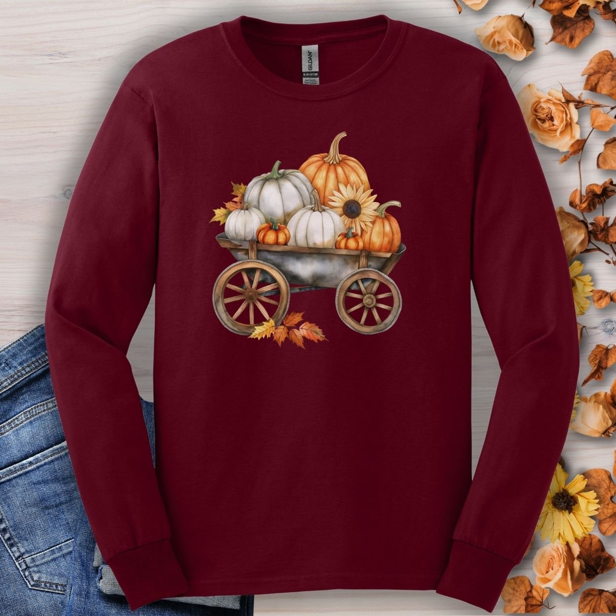 Maroon long-sleeve tee with a watercolor wagon full of white and orange pumpkins and fall leaves.