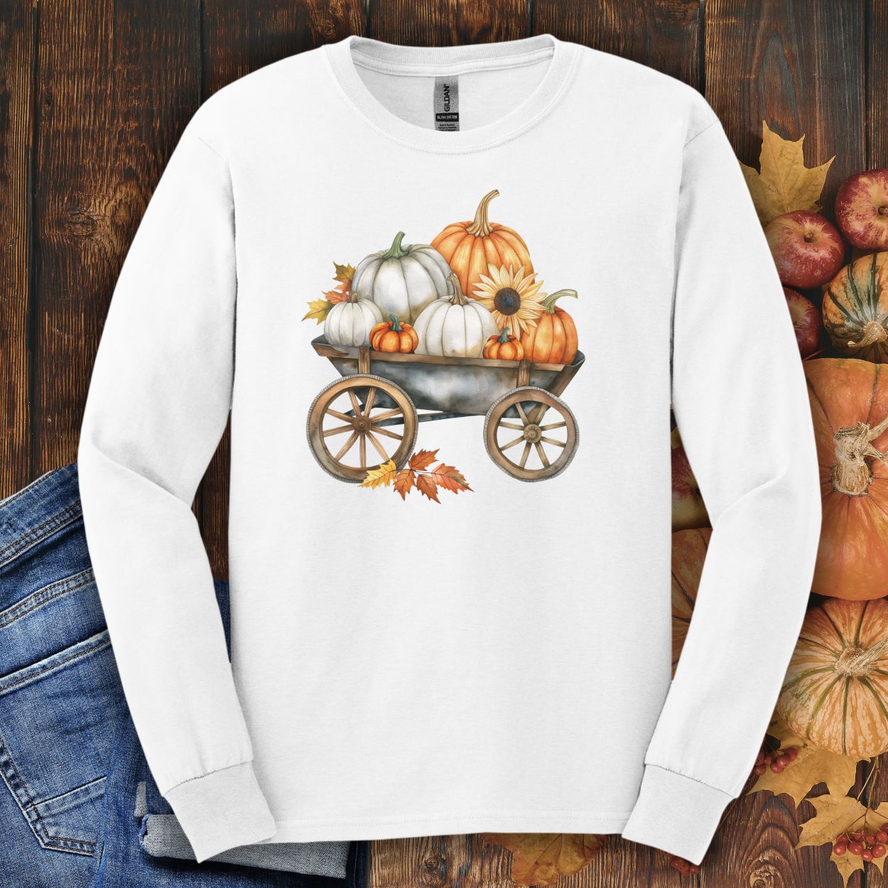 White long-sleeve tee with a watercolor wagon full of white and orange pumpkins and fall leaves.