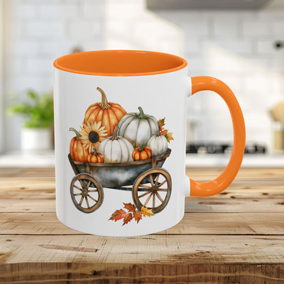 White ceramic mug with an orange rim and handle, featuring a watercolor-style autumn pumpkin harvest wagon design.