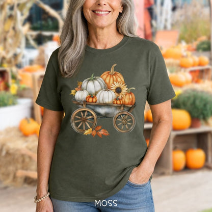 Woman wearing a moss green t-shirt with a rustic wagon full of watercolor pumpkins and sunflowers.