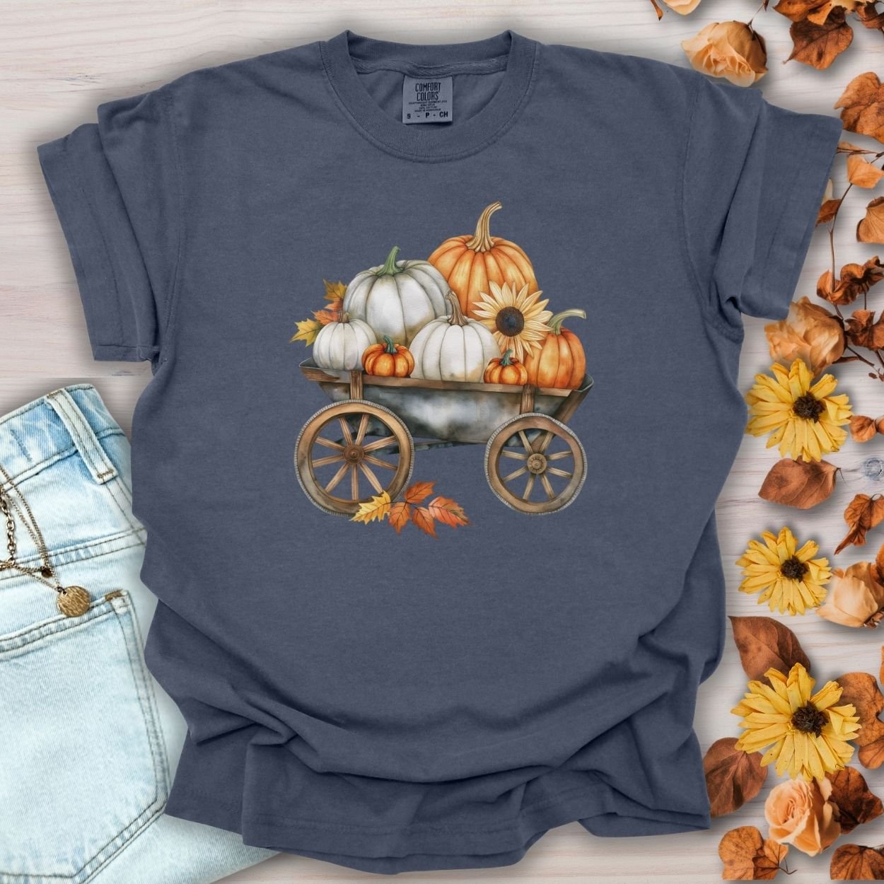 Denim blue garment-dyed cotton t-shirt with a watercolor rustic wagon piled with white and orange pumpkins, sunflowers, and autumn leaves.