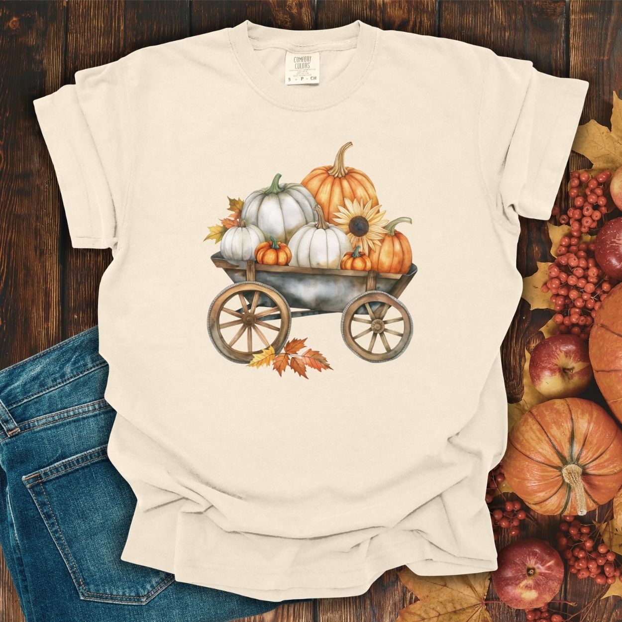 Ivory S-sized t-shirt with a watercolor rustic wagon filled with white and orange pumpkins, sunflowers, and fall leaves.
