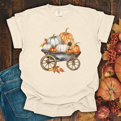 Ivory S-sized t-shirt with a watercolor rustic wagon filled with white and orange pumpkins, sunflowers, and fall leaves.