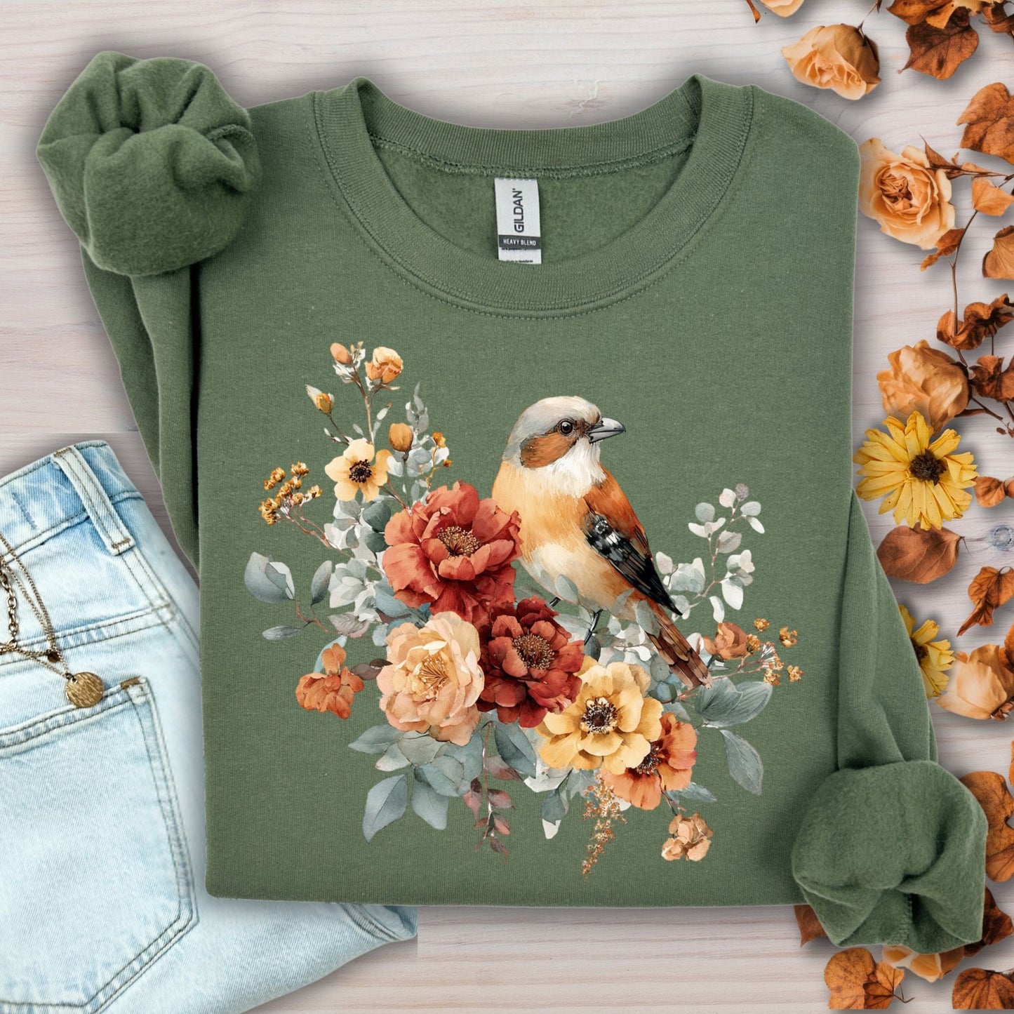 Military Green Gildan crewneck sweatshirt with watercolor sparrow and autumn roses, next to jeans and dried leaves.