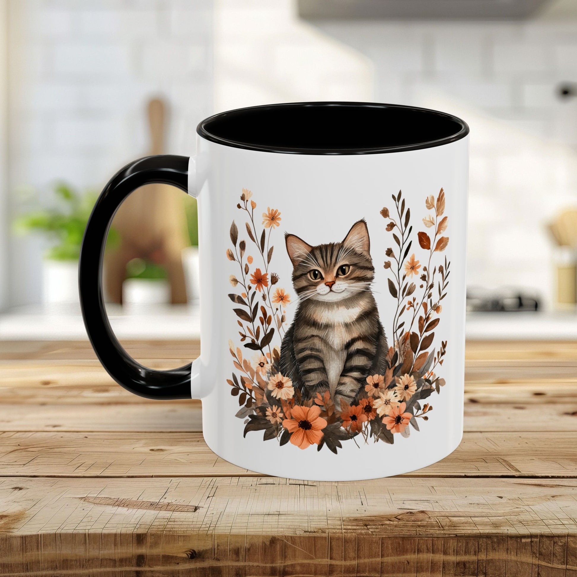 Glossy white ceramic mug with a tabby kitten surrounded by autumnal wildflowers, black interior and handle.
