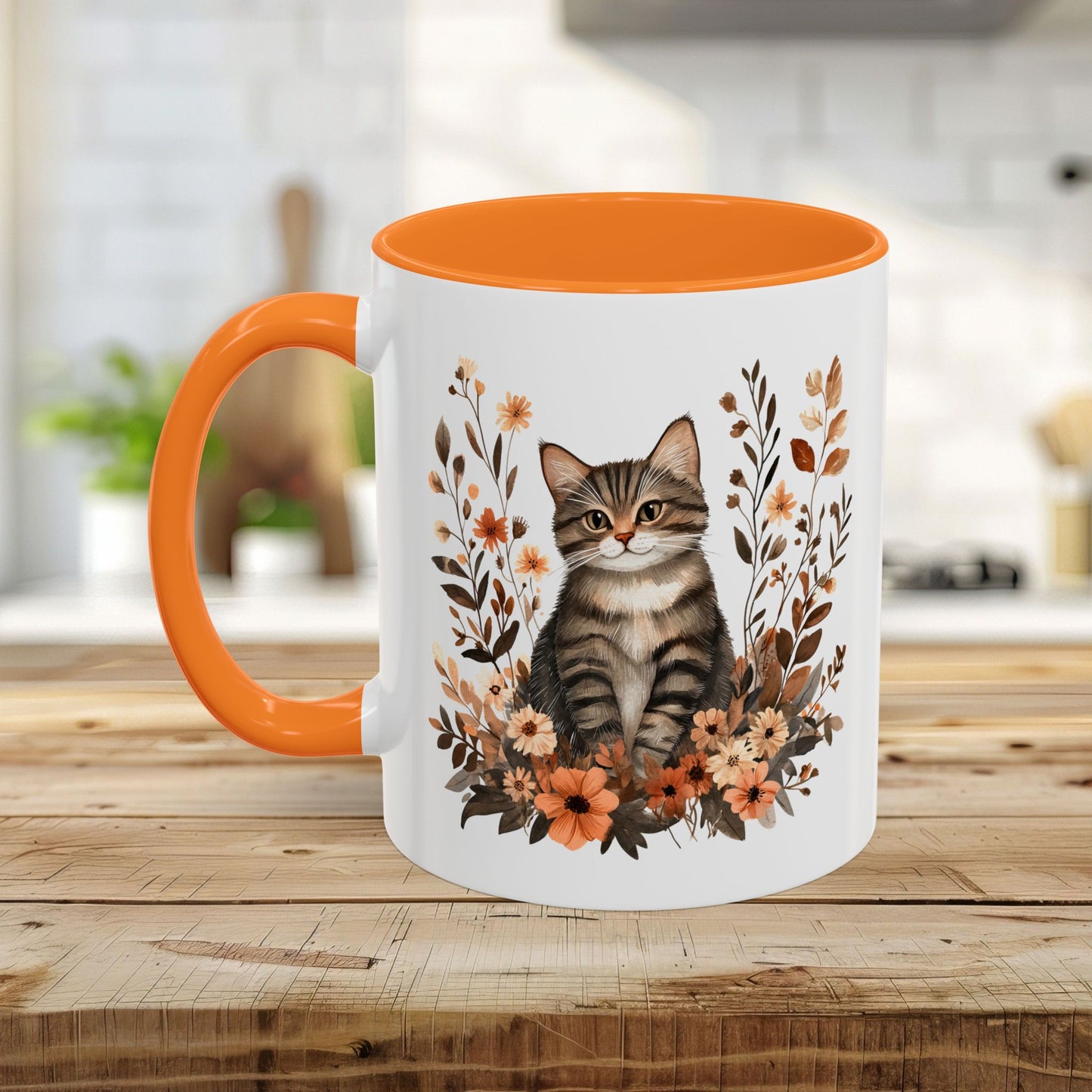 White ceramic mug with an orange interior and handle, featuring a striped tabby kitten surrounded by warm, autumnal wildflowers.