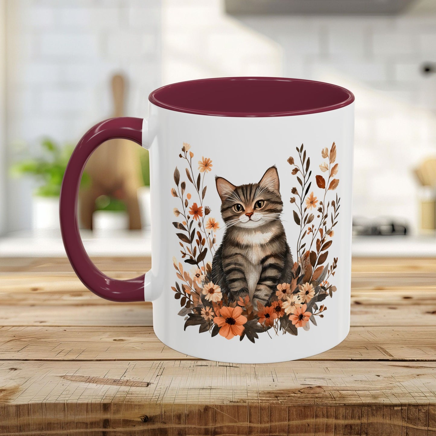 White ceramic mug with a tabby kitten surrounded by burnt orange and brown wildflowers, maroon interior and handle.