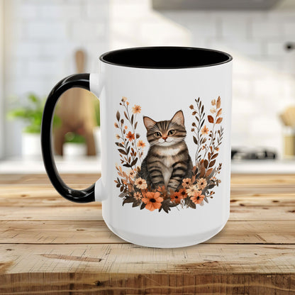 Glossy white ceramic mug with a black handle and interior, featuring a tabby cat surrounded by autumnal wildflowers.