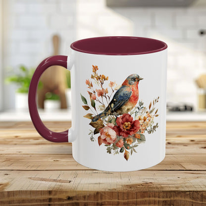 White ceramic mug with a watercolor bluebird and peony design, burgundy interior and C-shaped handle.