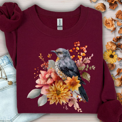 Maroon crewneck sweatshirt with a painterly bluebird and autumn floral design, made from a cotton-polyester blend.
