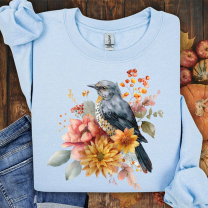 Light blue crewneck sweatshirt with a painterly bluebird and autumn floral design.