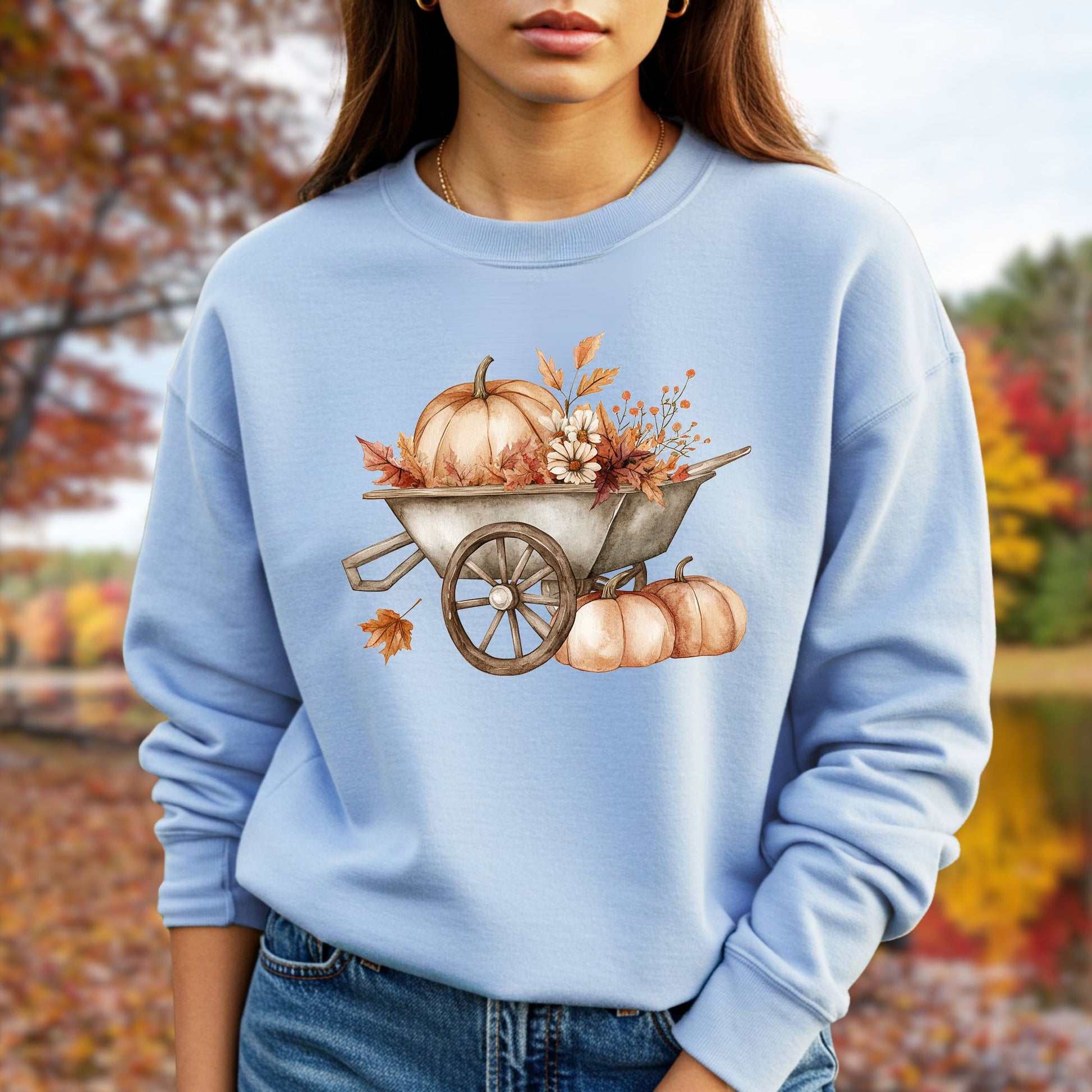 Light blue sweatshirt with a boho wagon full of pumpkins and autumn flowers, worn by a person outdoors.
