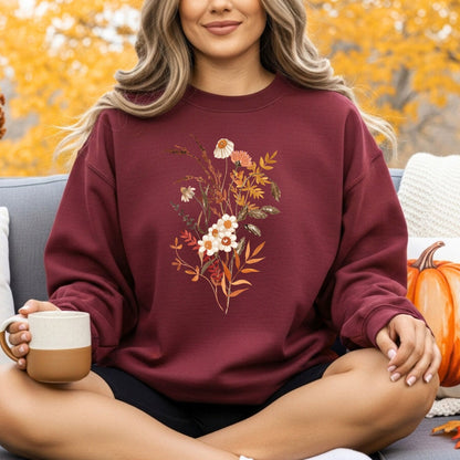 Woman in a maroon crewneck sweatshirt with a vintage autumn wildflower bouquet design, holding a mug.