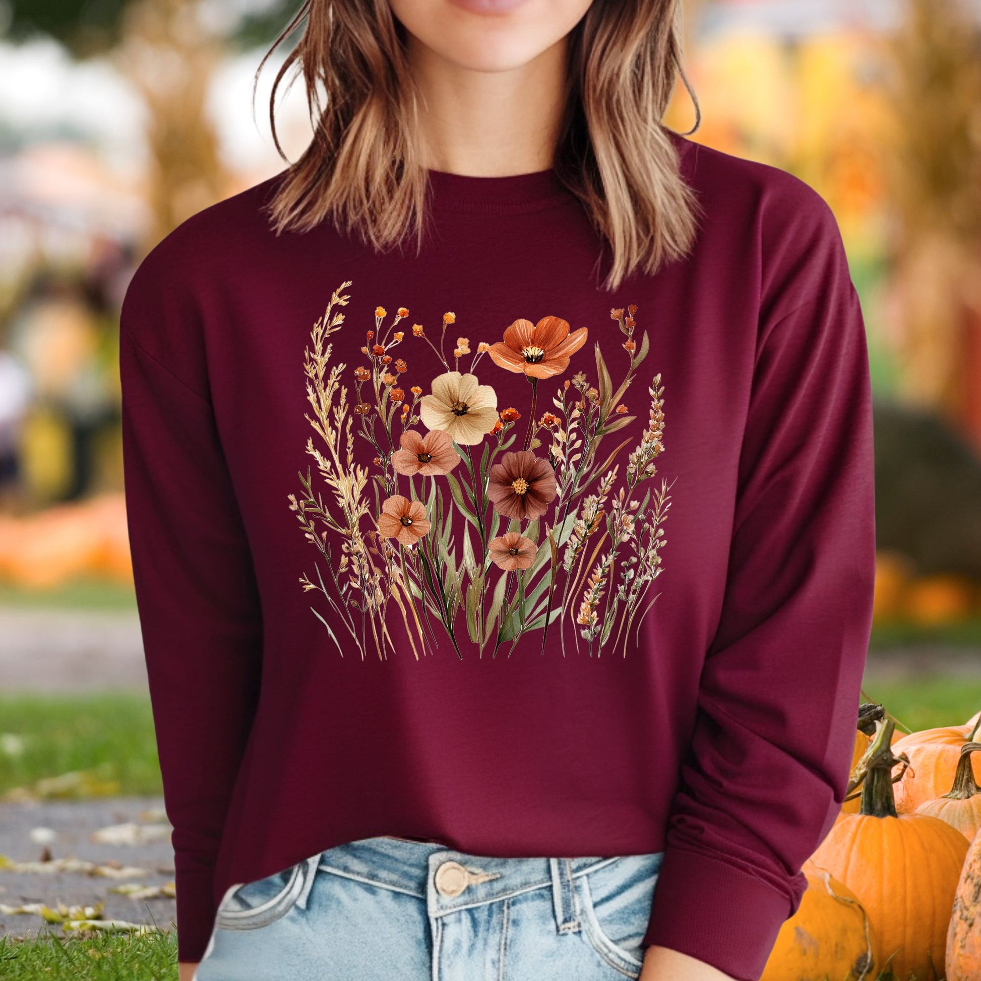 Maroon long-sleeve tee with watercolor autumn wildflowers in warm hues, worn by a woman outdoors.