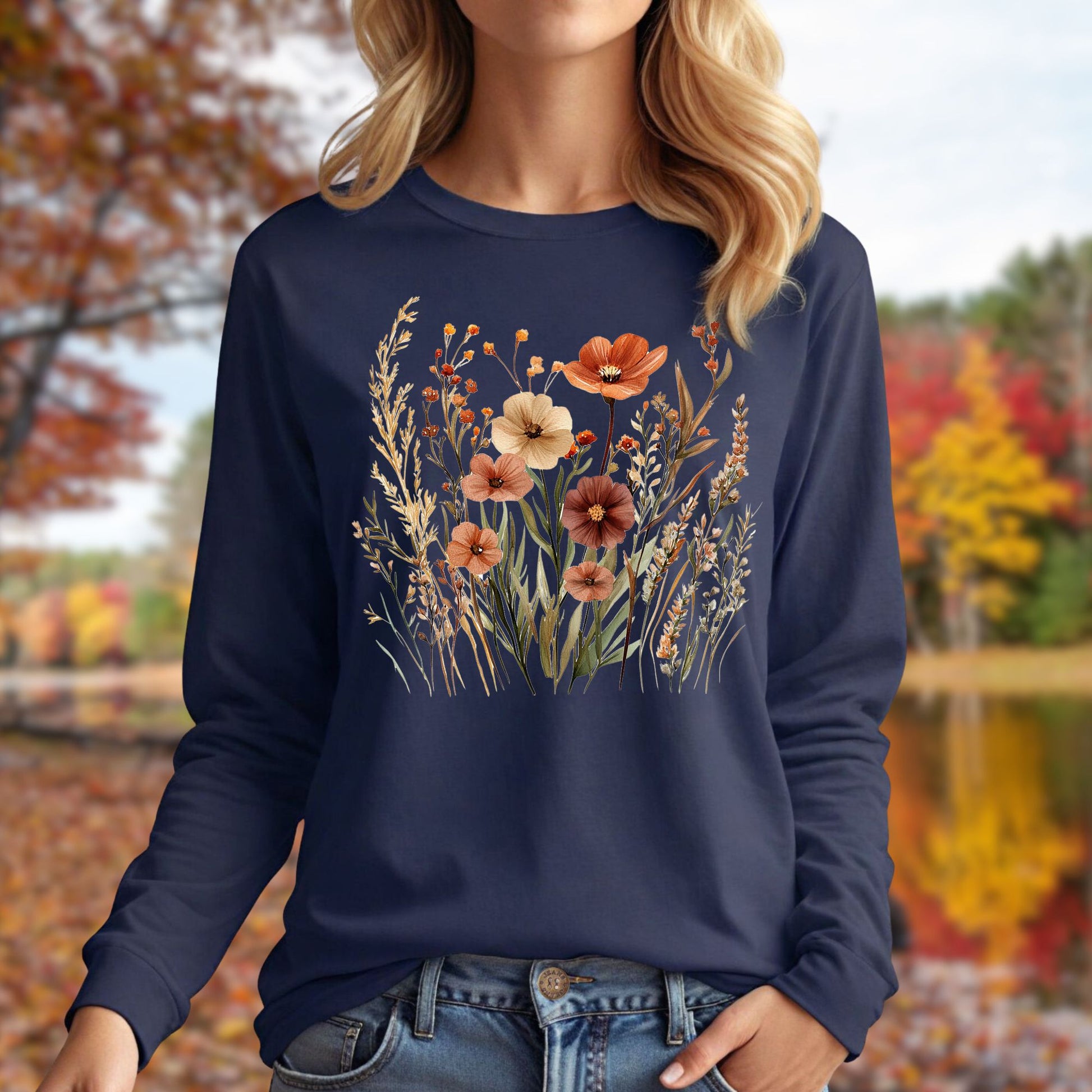 Navy long-sleeve tee with watercolor autumn wildflowers in warm hues, worn by a woman outdoors.