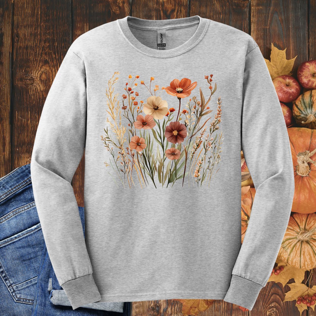 Ash long-sleeve tee with watercolor autumn wildflowers, shown with jeans, pumpkins, and fall leaves.