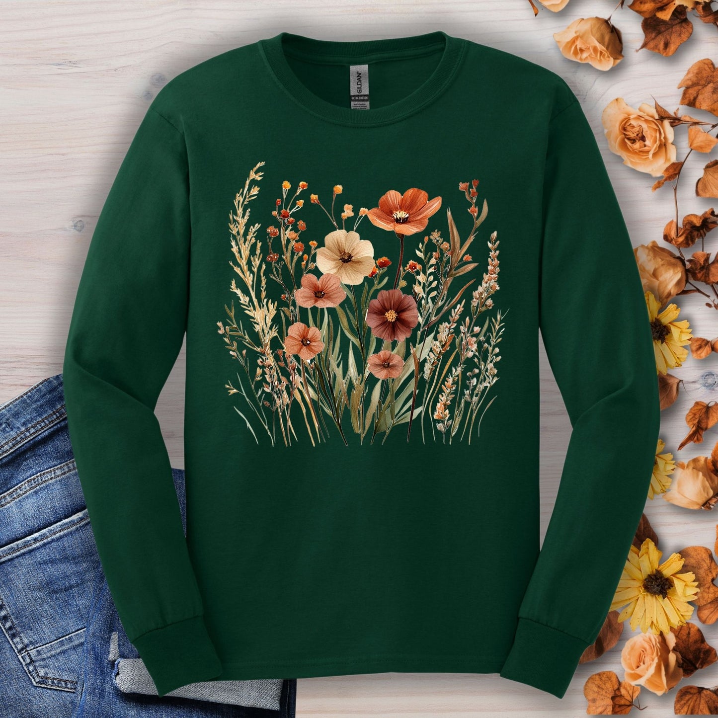 Forest Green long-sleeve tee with watercolor autumn wildflowers in warm hues, on a light wood background.