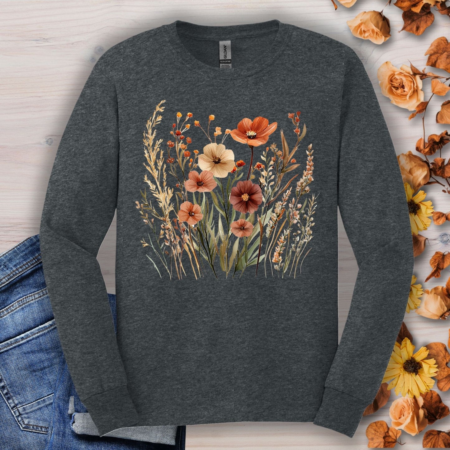 Dark Heather long-sleeve tee with watercolor autumn wildflowers, laid on wood with fall leaves.