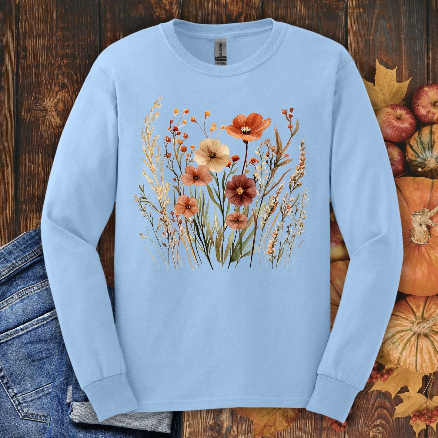 Light blue long-sleeve tee with watercolor autumn wildflowers, surrounded by fall leaves, apples, and pumpkins.