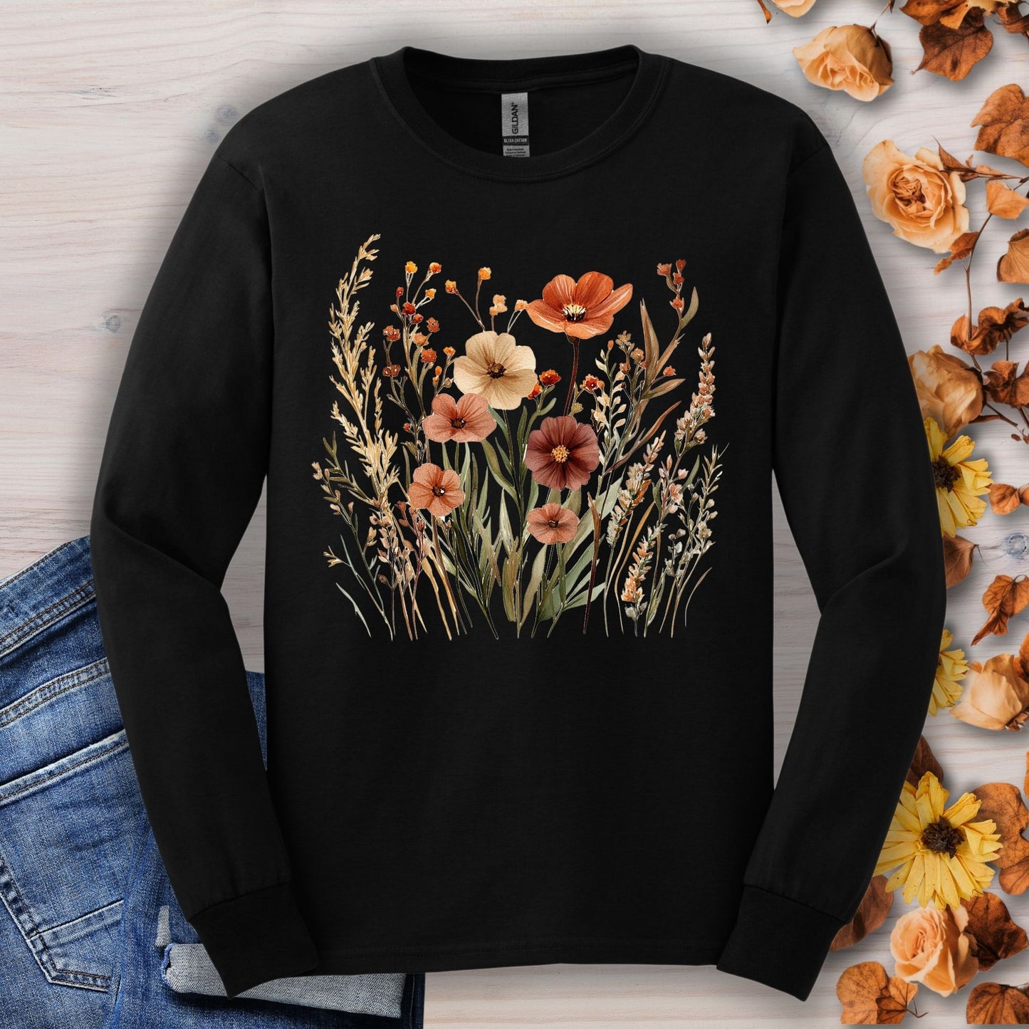 Black long-sleeve tee with watercolor autumn wildflowers in warm hues, shown with jeans and fall decor.