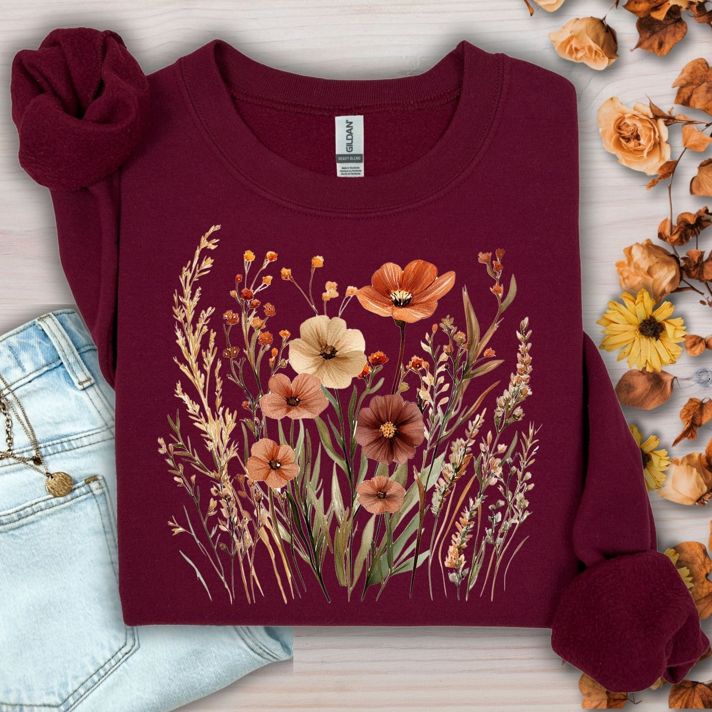 Maroon cotton-blend sweatshirt with watercolor autumn wildflowers and poppies design, next to jeans.